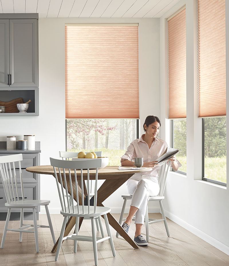 a woman sitting in her kitchen reading a newspaper with Hunter Douglas blinds covering the windows behind her