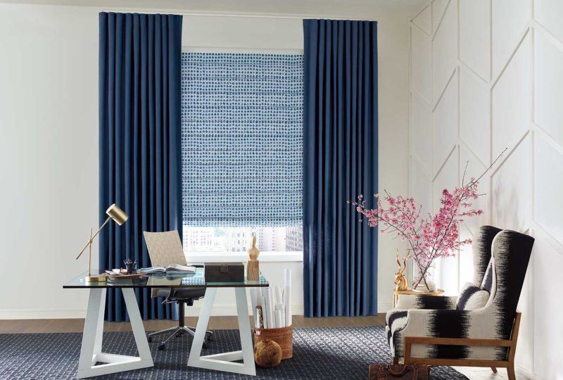 a desk in the middle of an office with floor length blue drapery and a Hunter Douglas blind covering the window