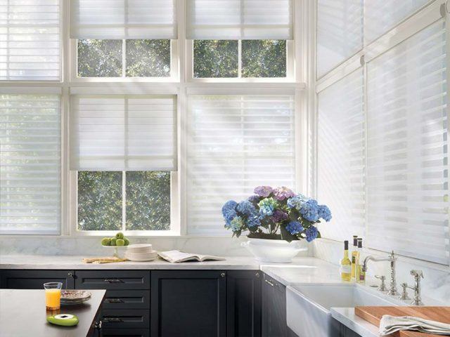 a kitchen with large windows that have Hunter Douglas motorized white blinds