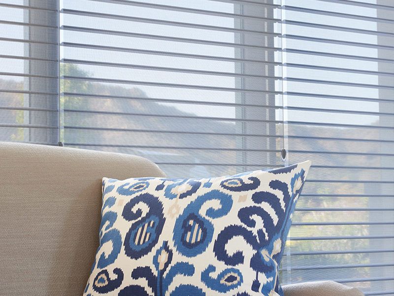 Hunter Douglas silhouette blinds behind a couch with a blue accent pillow