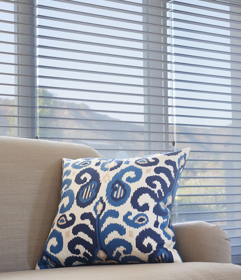 Hunter Douglas silhouette blinds behind a couch with a blue accent pillow