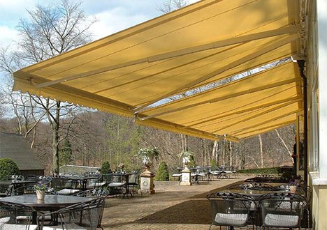 a patio with several empty tables, being covered in shade from three retractable awnings