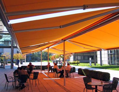 a patio being covered in shade by large yellow stand alone awnings