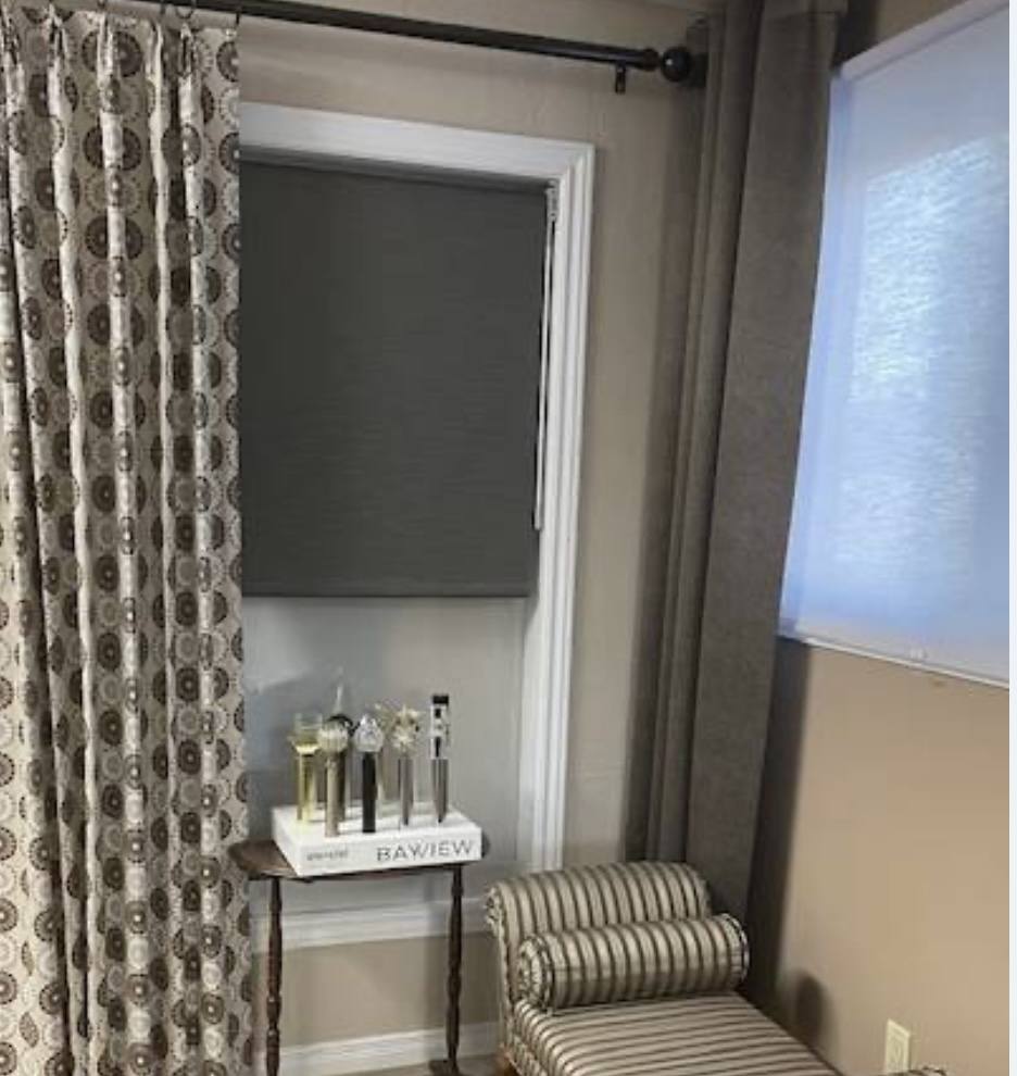 Window with layered curtains, roller shade, side table, and striped bench.